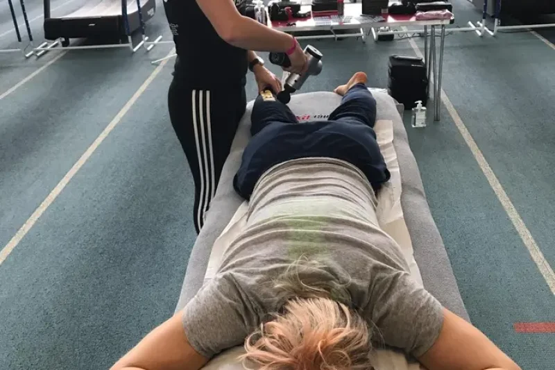 A person receiving percussion massage therapy on their lower back using a handheld massage device.
